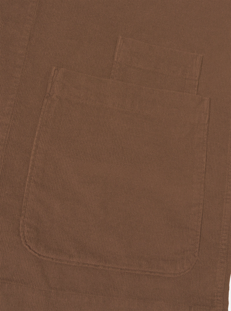 A detailed close-up shot of the Universal Works Brown Fine Cord Bakers Overshirt on a plain white background, highlighting the fine-wale corduroy texture, front patch pocket, and tonal button placket.