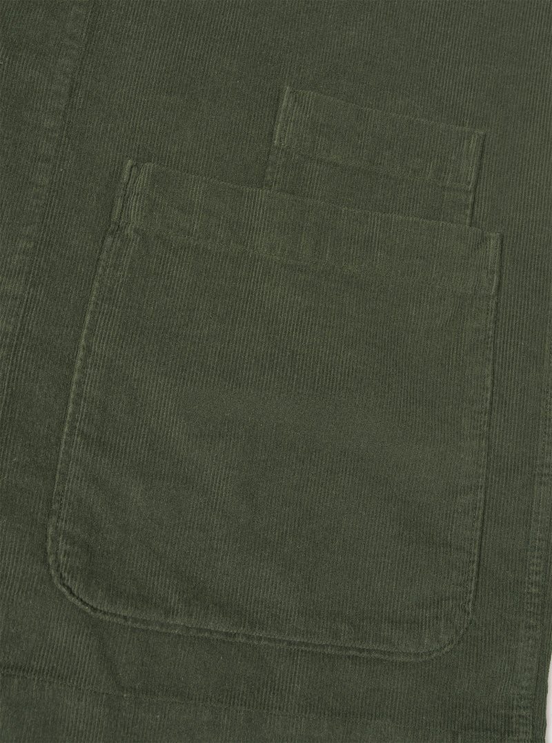 A close-up detail shot of the Universal Works Olive Fine Cord Bakers Overshirt on a plain white background, highlighting the fine-wale cotton corduroy texture, front buttons, and chest pocket.