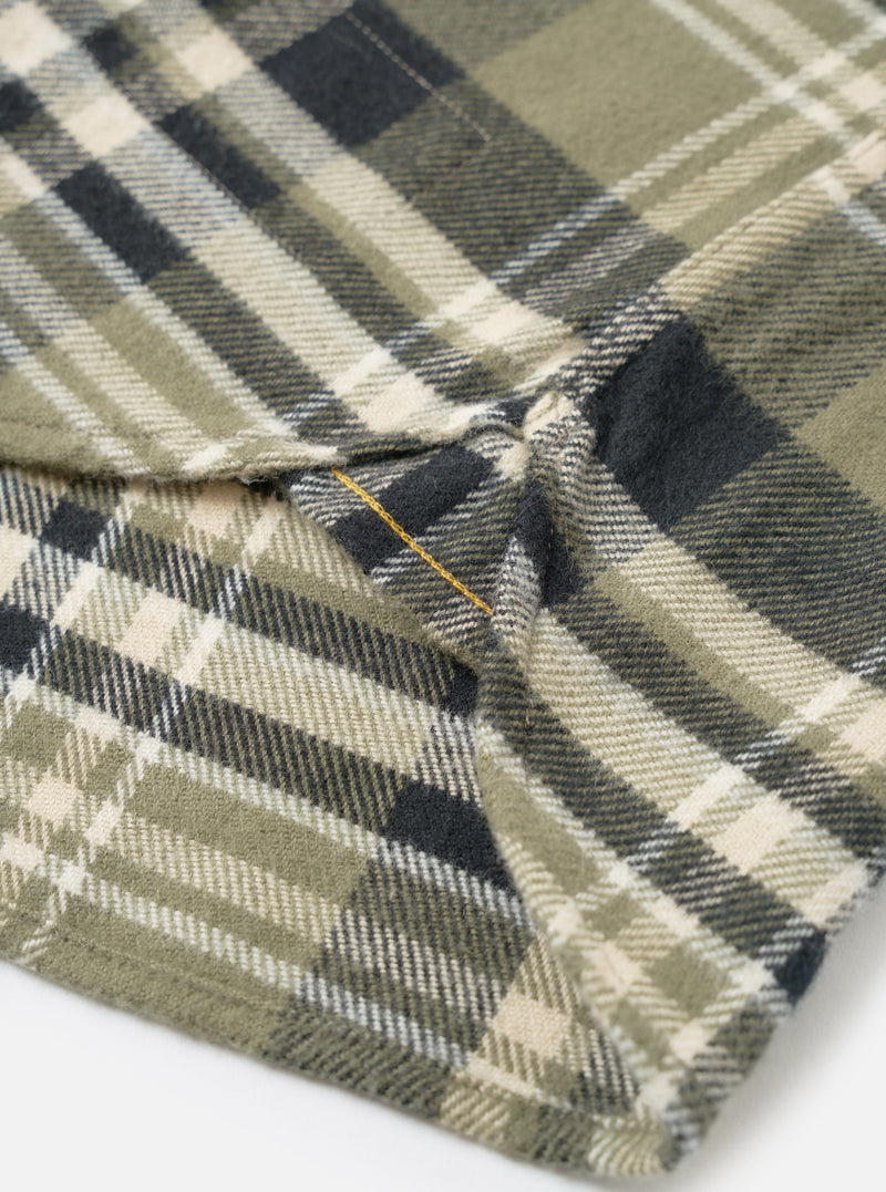 A side profile view of a male model wearing the Universal Works Olive Jazz Check Standard Shirt against a plain backdrop, featuring the buttoned cuffs, clean sleeve line, and subtle checked pattern.