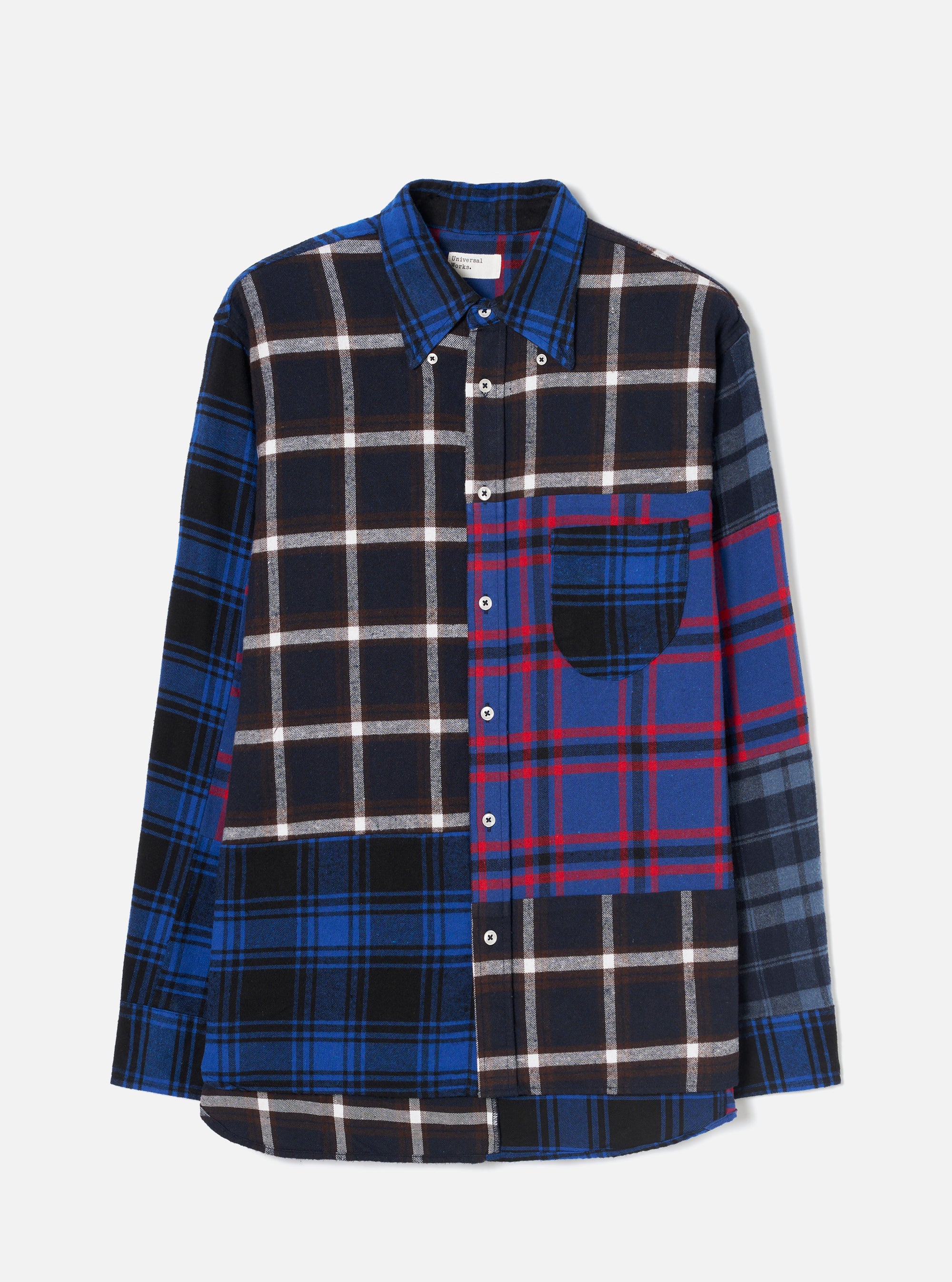 Blue patchwork flannel shirt laid flat on a light grey backdrop. Four contrasting check panels are cut and sewn together: navy and white on the left body and sleeve, blue and red tartan on the right body, and grey and blue check on the right sleeve. Point collar, button-down placket with silver buttons, single chest patch pocket, and a curved hem.