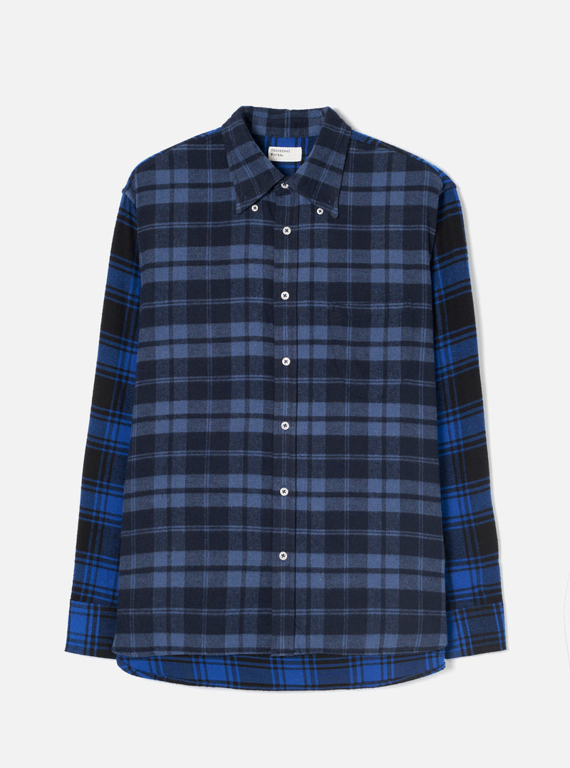 Flat lay of a Universal Works navy and blue brushed flannel check shirt on a light grey studio backdrop. The body features a navy and slate check while the sleeves and hem panel use a contrasting bright blue, black and navy tartan. Point collar with button-down tabs, white buttons down the placket, a chest patch pocket, and a curved shirttail hem.