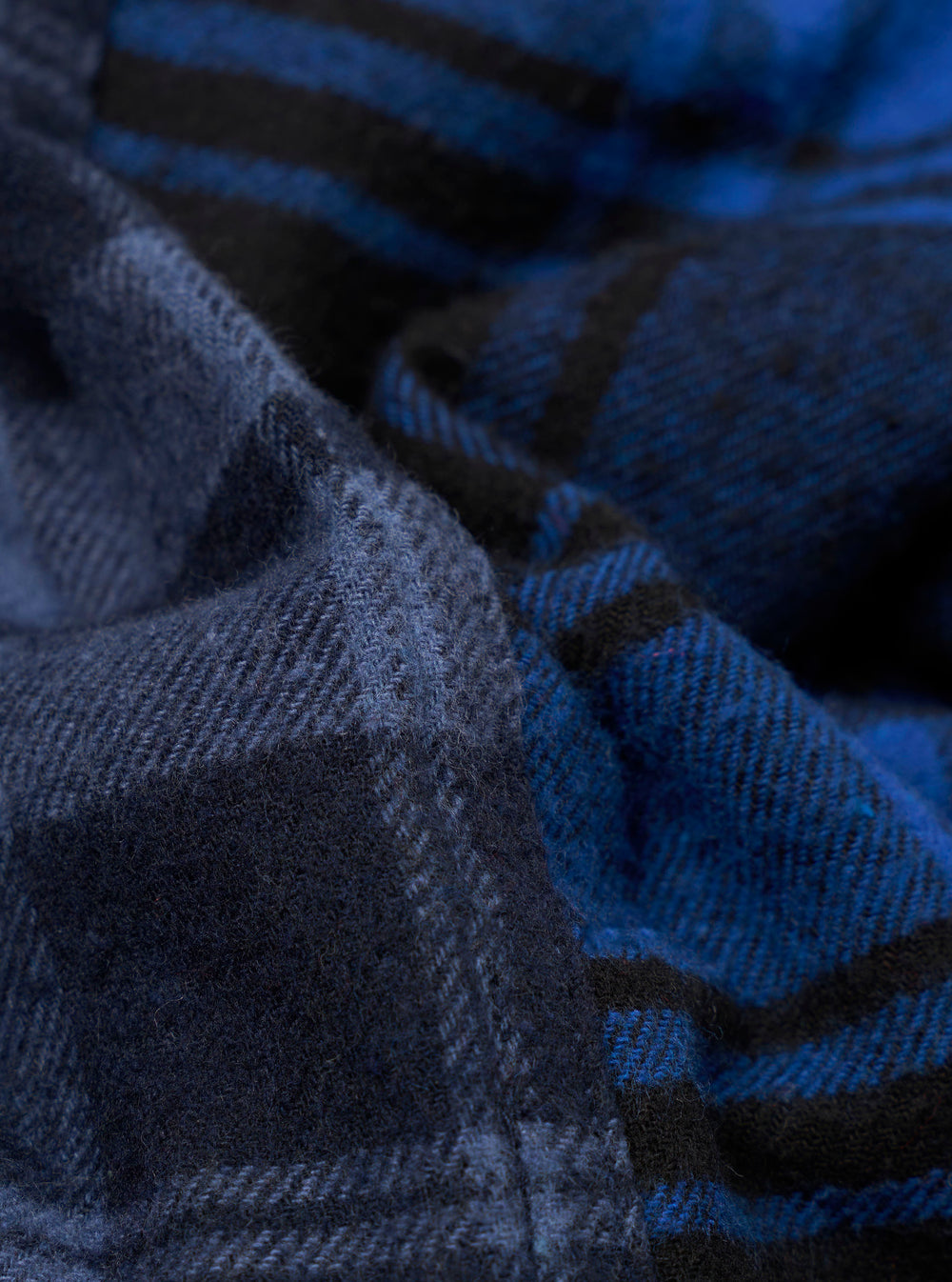 Close-up fabric detail of the navy and blue brushed panel check shirt. The woven check pattern features deep navy, cobalt blue and black tones with a soft, brushed texture visible across the draped fabric folds. No model or mannequin is present.