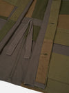 Close-up flat lay of an olive patchwork twill fatigue jacket showing the front placket and lower body. Patchwork panels in olive, khaki brown and charcoal grey are visible. A herringbone twill tape tie is knotted at the waist opening. Two vertical buttonholes are visible on the right placket. Stitched hem detail shows at the bottom edge.