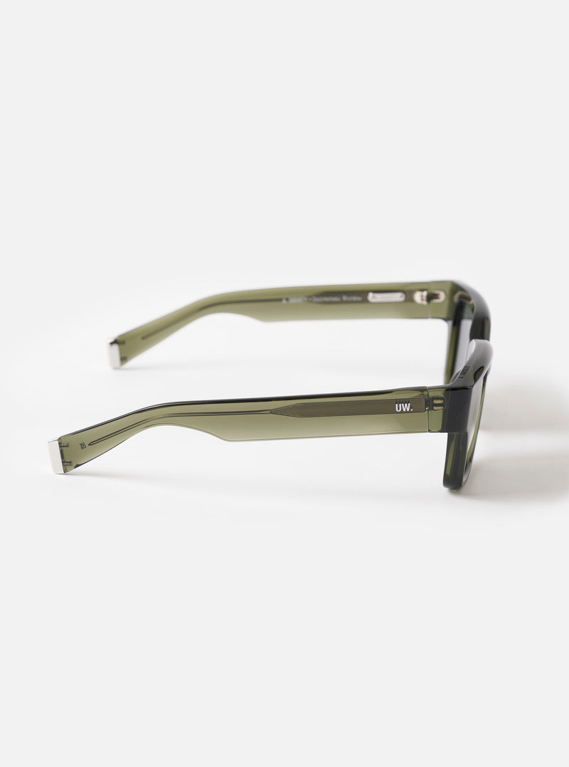 Three-quarter angle studio view of the A. SOCIETY x Universal Works Olive Hollywood Sunglasses on a light white background, showcasing the rich olive frame color, sleek curves, and dark tinted lenses.