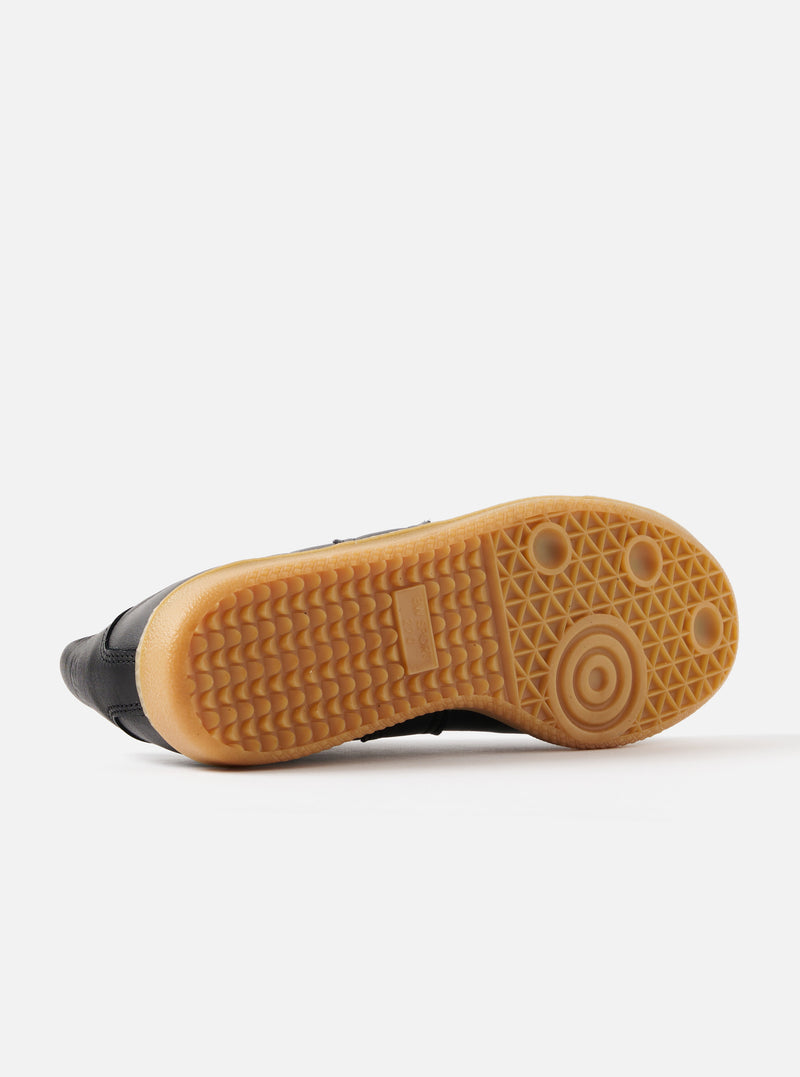 Close-up of the sole of a Novesta for Universal Works Black Leather German Army Trainer. The sole is tan with a textured grip. Shot on a white background.