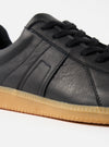 Close-up of the Novesta for Universal Works Black Leather German Army Trainer. Features black leather upper, black laces, and a gum sole. Shot on a white background.