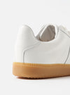 Close-up of the Novesta for Universal Works Off-White/White Leather German Army Trainer. Features white leather upper and gum sole. Shot in a clean, white studio setting.