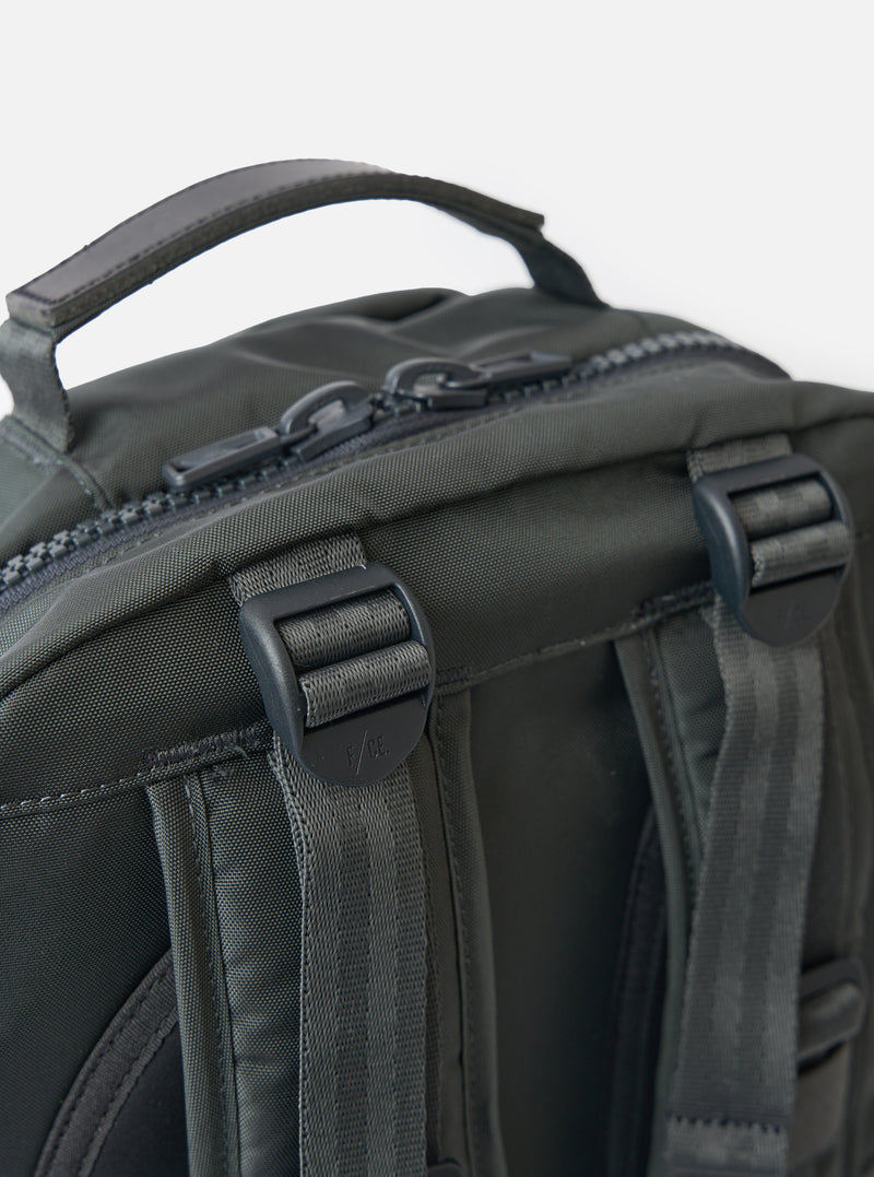 Close-up of the F/CE.® Grey Recycled Nylon 420 re/cor Travel Backpack. Shows grey nylon material, black zippers and straps. Shot against a white background.