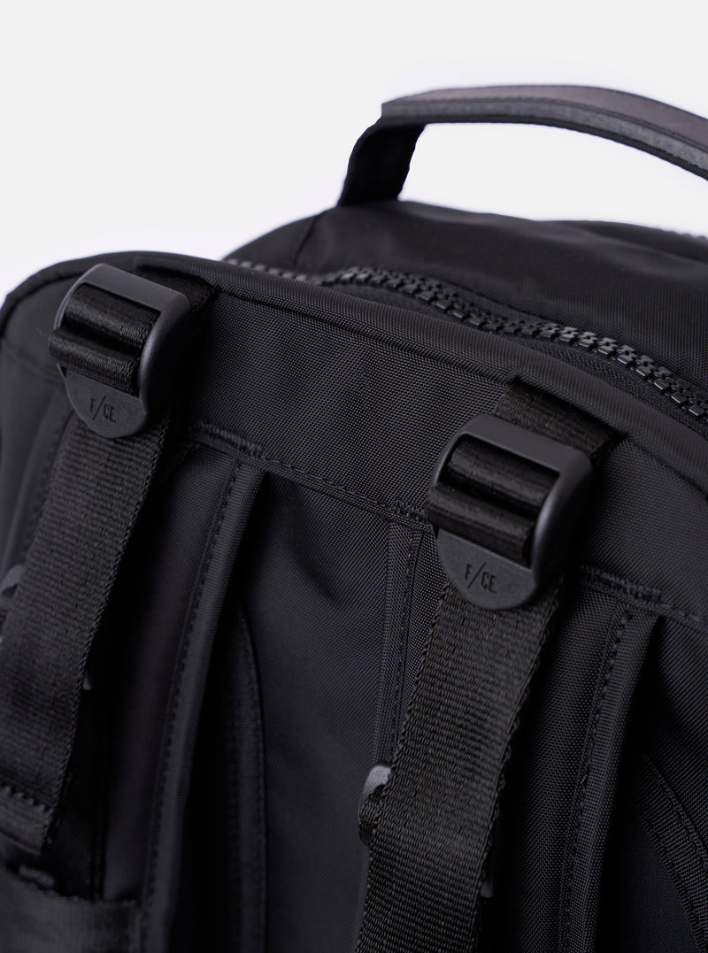 The F/CE.® Black Recycled Nylon 420 re/cor Travel Backpack is shown from a rear angle, highlighting the padded back panel made of black neoprene and the ergonomic shoulder straps. The straps feature the Mounting T System with nylon webbing for attachments and an adjustable chest buckle. The backpack is displayed as a flat lay against a plain white background.