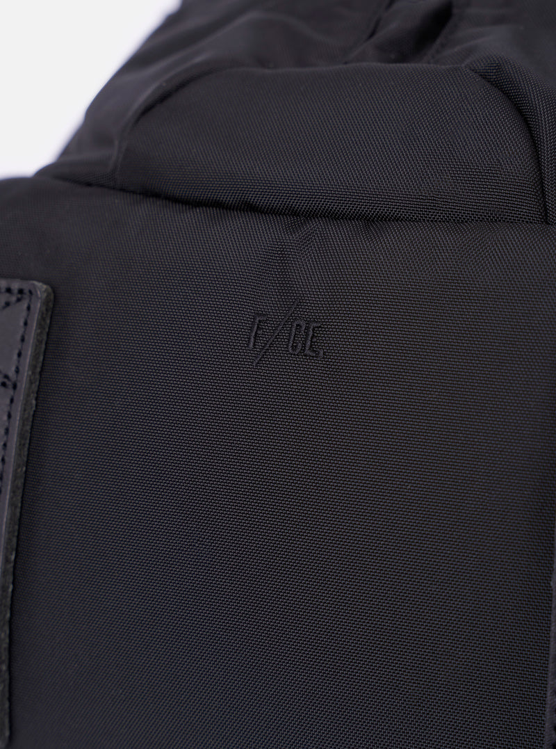 The F/CE. Black Recycled Nylon 420 re/cor Travel Backpack is shown from the back as a flat lay against a plain white background. The image highlights the padded mesh back panel, the ergonomically curved shoulder straps with adjustable webbing, and the top carry handle. The black recycled nylon fabric has a subtle sheen.