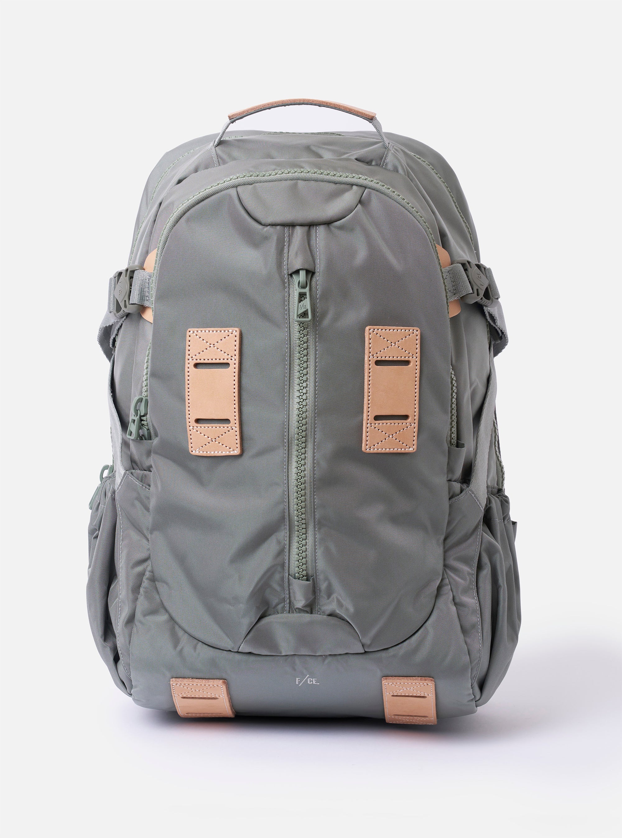 The F/CE.® Foliage Green Recycled Nylon 420 re/cor Travel Backpack is shown from a front angle against a plain white background. The backpack features a multi-pocket design with a prominent front gadget pocket, adjustable shoulder straps equipped with a mounting system, and a top haul handle. The foliage green recycled nylon fabric has a subtle sheen, and black hardware and buckles provide a functional contrast.