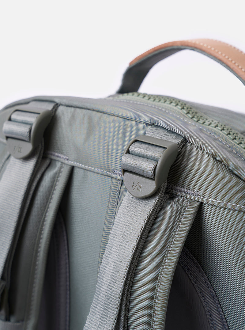 The F/CE.® Foliage Green Recycled Nylon 420 re/cor Travel Backpack is shown from a rear angle as a flat lay against a plain white background. The image highlights the padded back panel made of black neoprene and the ergonomic shoulder straps, which feature a technical mounting system for accessories. The foliage green recycled nylon fabric has a subtle sheen, and a small black brand label is visible at the bottom.