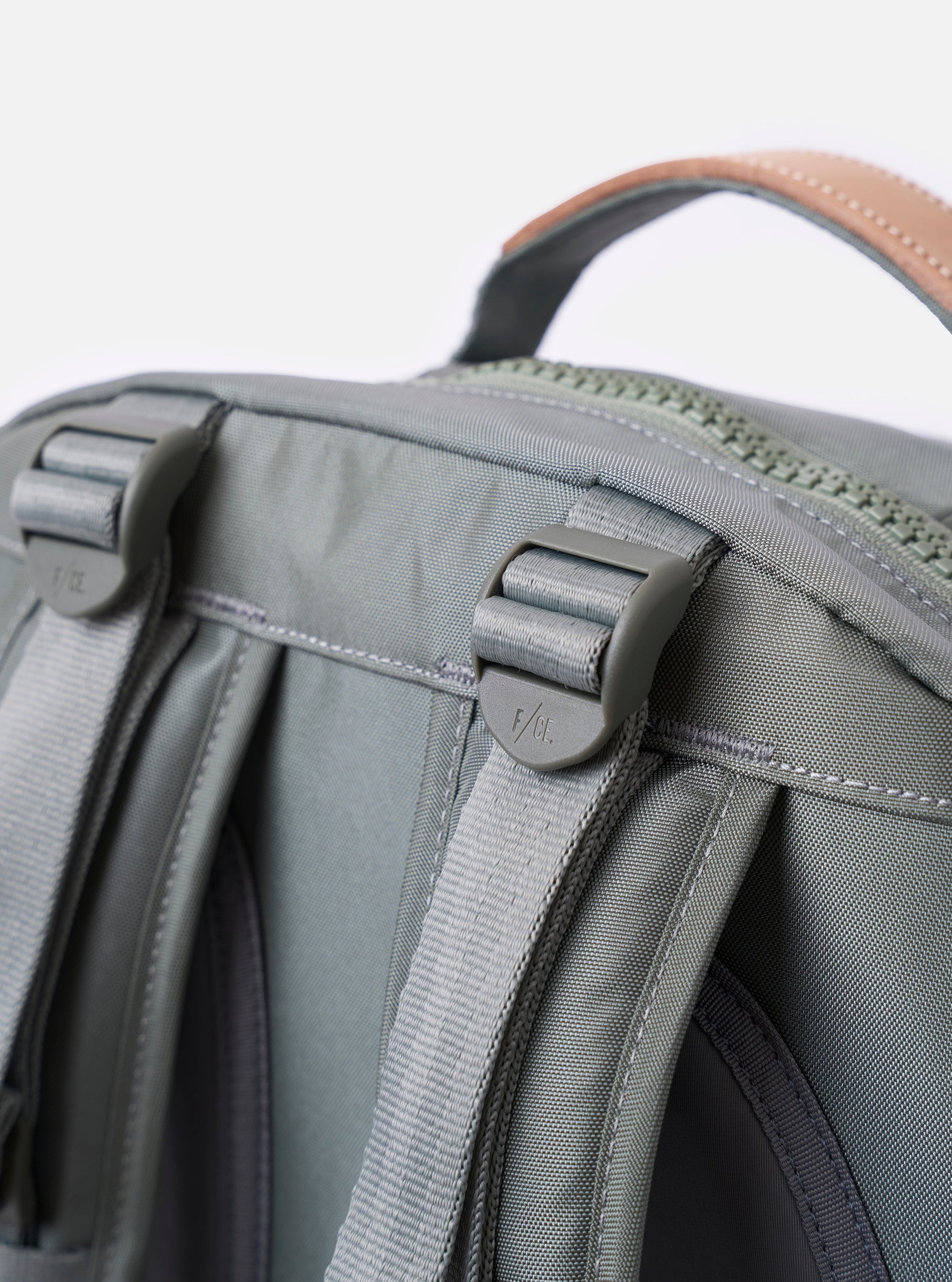 The F/CE.® Foliage Green Recycled Nylon 420 re/cor Travel Backpack is shown from a rear angle as a flat lay against a plain white background. The image highlights the padded back panel made of black neoprene and the ergonomic shoulder straps, which feature a technical mounting system for accessories. The foliage green recycled nylon fabric has a subtle sheen, and a small black brand label is visible at the bottom.