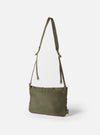 The F/CE.® Sage Green 420 re/cor Sacoche bag in sage green, hanging against a white background. The bag has a long strap and a small logo tag.