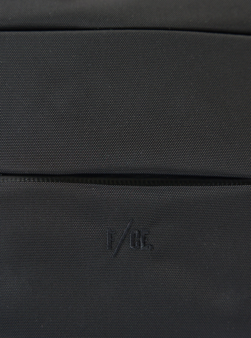 Close-up of the F/CE.® Black 420 re/cor Sacoche. The black textured material is visible. The F/CE logo is embroidered on the bottom. Shot on a flat surface.