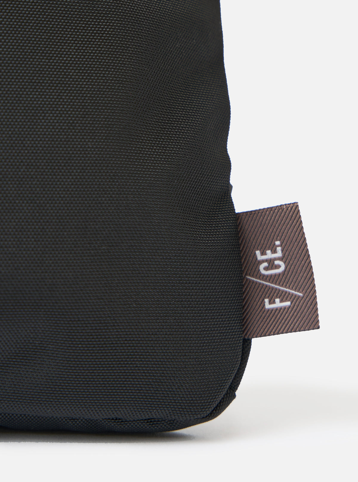 Close up of the F/CE.® Black 420 re/cor Sacoche showing the black textured material and the brown F/CE. tag on a white background.