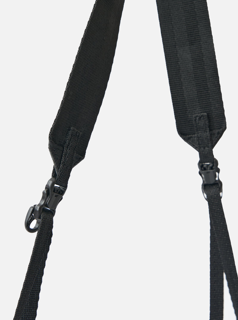 Close-up of the black straps and plastic buckles of the F/CE.® Black 420 re/cor Sacoche against a white background. The straps are made of a woven material.