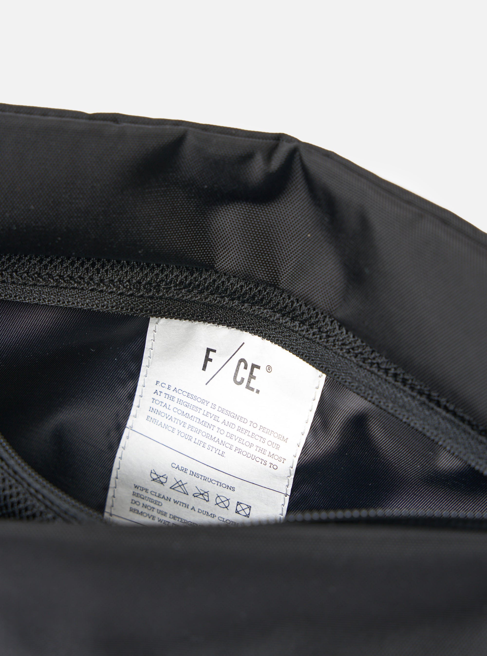 Close-up of the F/CE.® Black 420 re/cor Sacoche interior, showing the black material and a white care instructions tag. Shot on a white background.