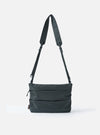 The F/CE.® Grey 420 re/cor Sacoche bag on a white background. The grey bag has a long adjustable strap. The bag is made of a durable material with a subtle texture.