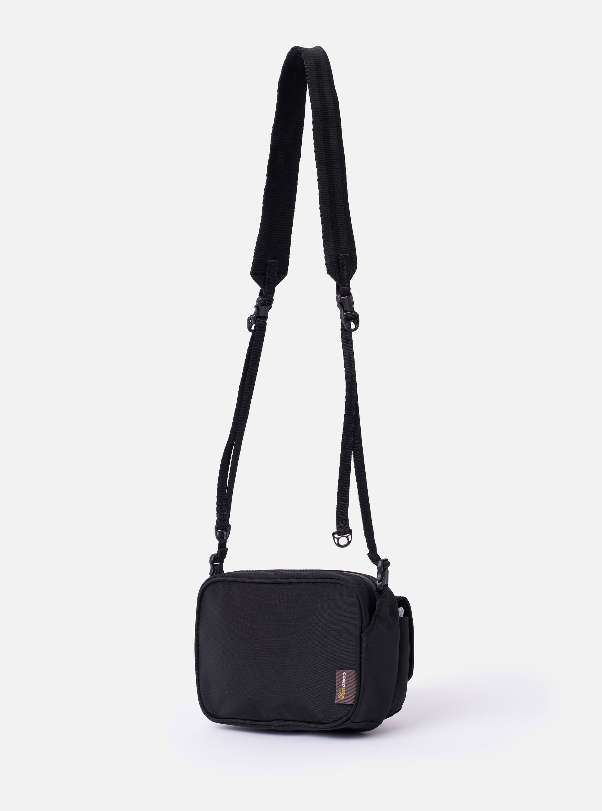 The F/CE. Black Recycled Nylon 420 re/cor Holiday Sacoche is shown from a side angle as a flat lay against a plain white background. The image highlights the slim profile of the bag, the adjustable black shoulder strap with plastic hardware, and the smooth, slightly lustrous texture of the black recycled nylon fabric.