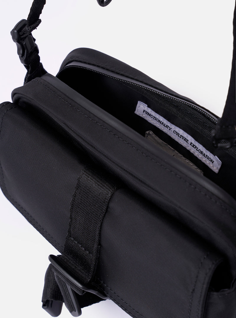 The F/CE. Black Recycled Nylon 420 re/cor Holiday Sacoche is shown from a rear angle against a plain white background. The image highlights the adjustable black shoulder strap attached with plastic buckles and the smooth, high-density weave of the black recycled nylon fabric.