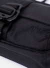 The F/CE.® Black Recycled Nylon 420 re/cor Holiday Sacoche is shown in a detail view as a flat lay against a plain white background. The image highlights the smooth black recycled nylon fabric, focusing on the two-compartment design and the clean stitching of the front pocket. A slim, adjustable black shoulder strap and a small embroidered logo are visible.