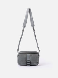 The F/CE.® Foliage Green Recycled Nylon 420 re/cor Holiday Sacoche is shown as a flat lay against a white background. The small, rectangular shoulder bag features two main zippered compartments, an adjustable black cord shoulder strap with plastic hardware, and a small brand label on the front. The foliage green fabric has a smooth, technical appearance.