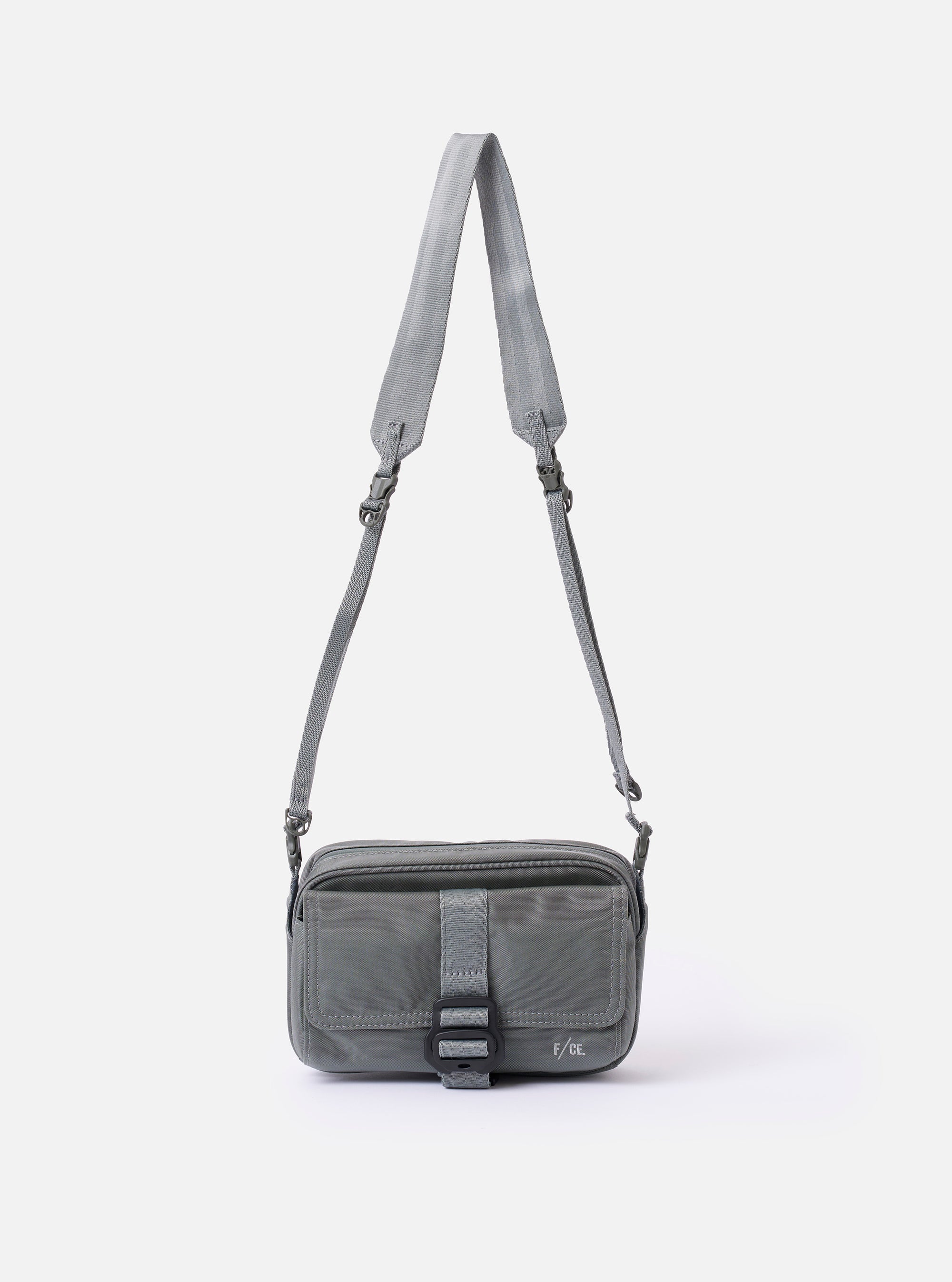The F/CE.® Foliage Green Recycled Nylon 420 re/cor Holiday Sacoche is shown as a flat lay against a white background. The small, rectangular shoulder bag features two main zippered compartments, an adjustable black cord shoulder strap with plastic hardware, and a small brand label on the front. The foliage green fabric has a smooth, technical appearance.