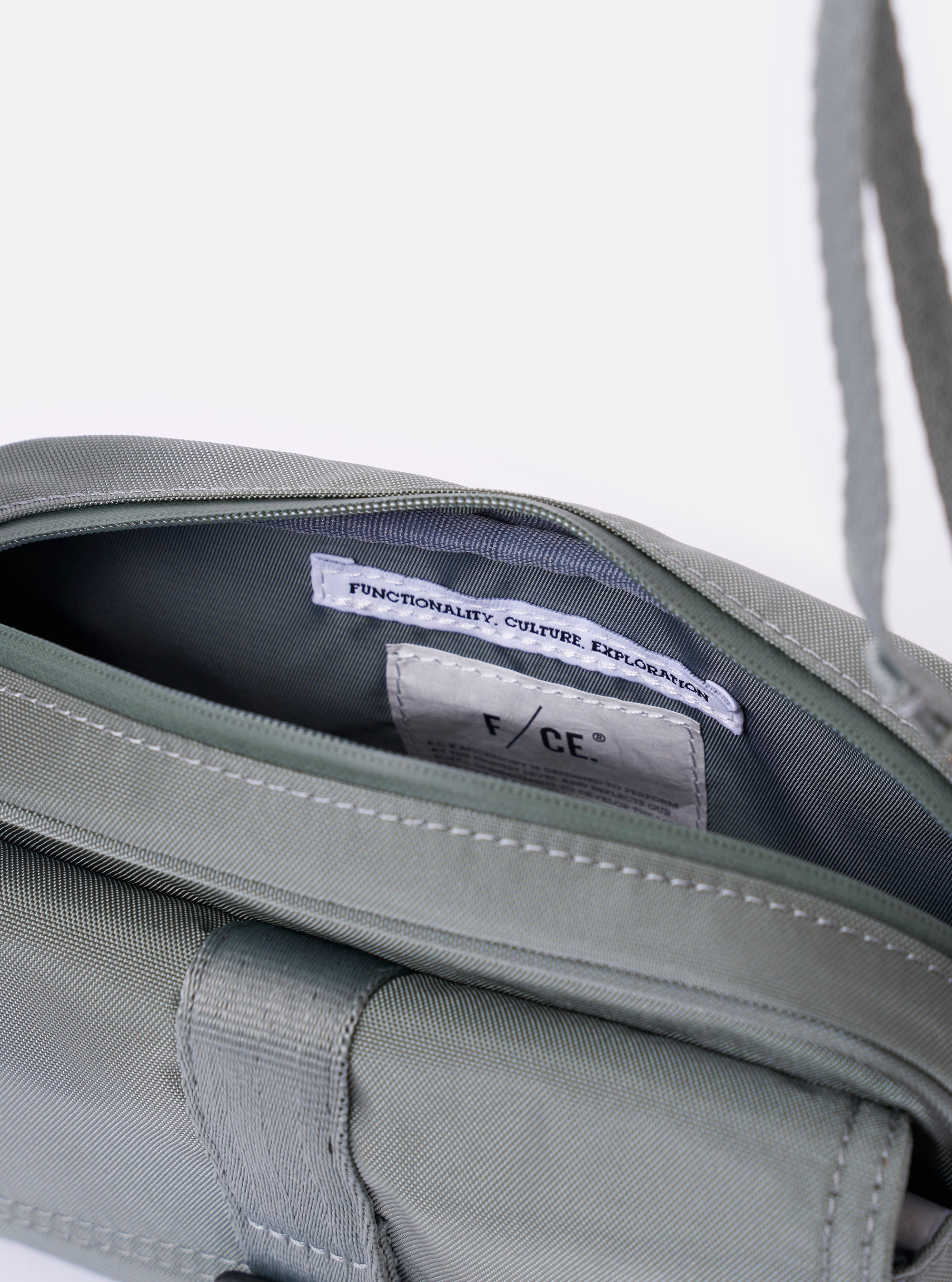 The F/CE.® Foliage Green Recycled Nylon 420 re/cor Holiday Sacoche is shown as a flat lay against a white background. The small messenger-style bag features a front pocket with a flap closure, a main zippered compartment, and an adjustable shoulder strap made of webbing. The foliage green recycled nylon fabric has a smooth, technical finish.