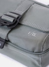 The F/CE.® Foliage Green Recycled Nylon 420 re/cor Holiday Sacoche is shown from a rear angle as a flat lay against a plain white background. The image highlights the back of the small bag, featuring a black adjustable shoulder strap with a plastic buckle and a loop for attachments. The foliage green recycled nylon fabric has a smooth, technical appearance.