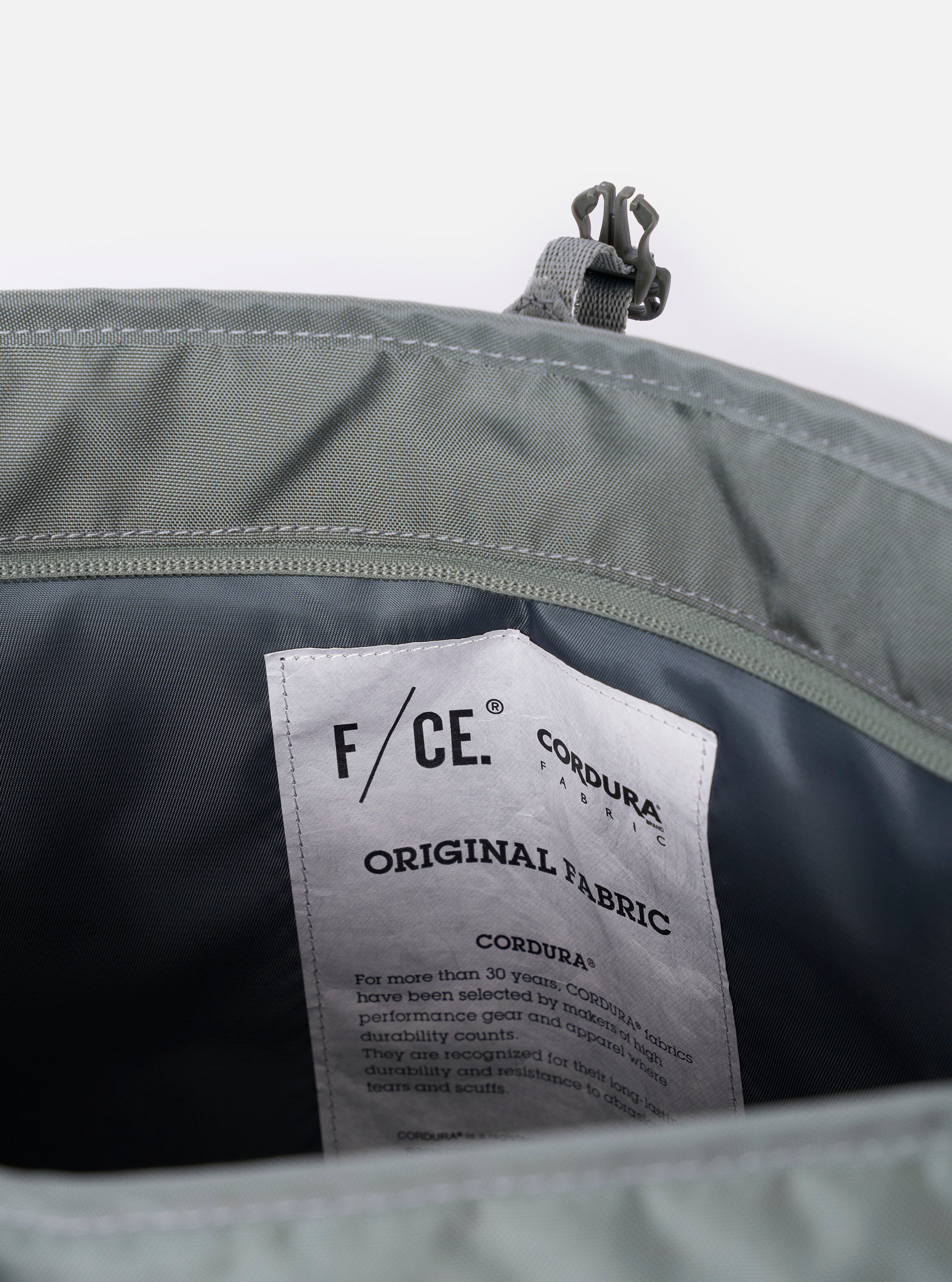 The F/CE.® Foliage Green Recycled Nylon 420 re/cor Courier Shoulder Bag is shown from a rear angle as a flat lay against a plain white background. This view highlights the adjustable messenger-style shoulder strap with its plastic buckle and the padded mesh back panel designed for comfort. The foliage green recycled nylon fabric has a smooth, technical appearance.