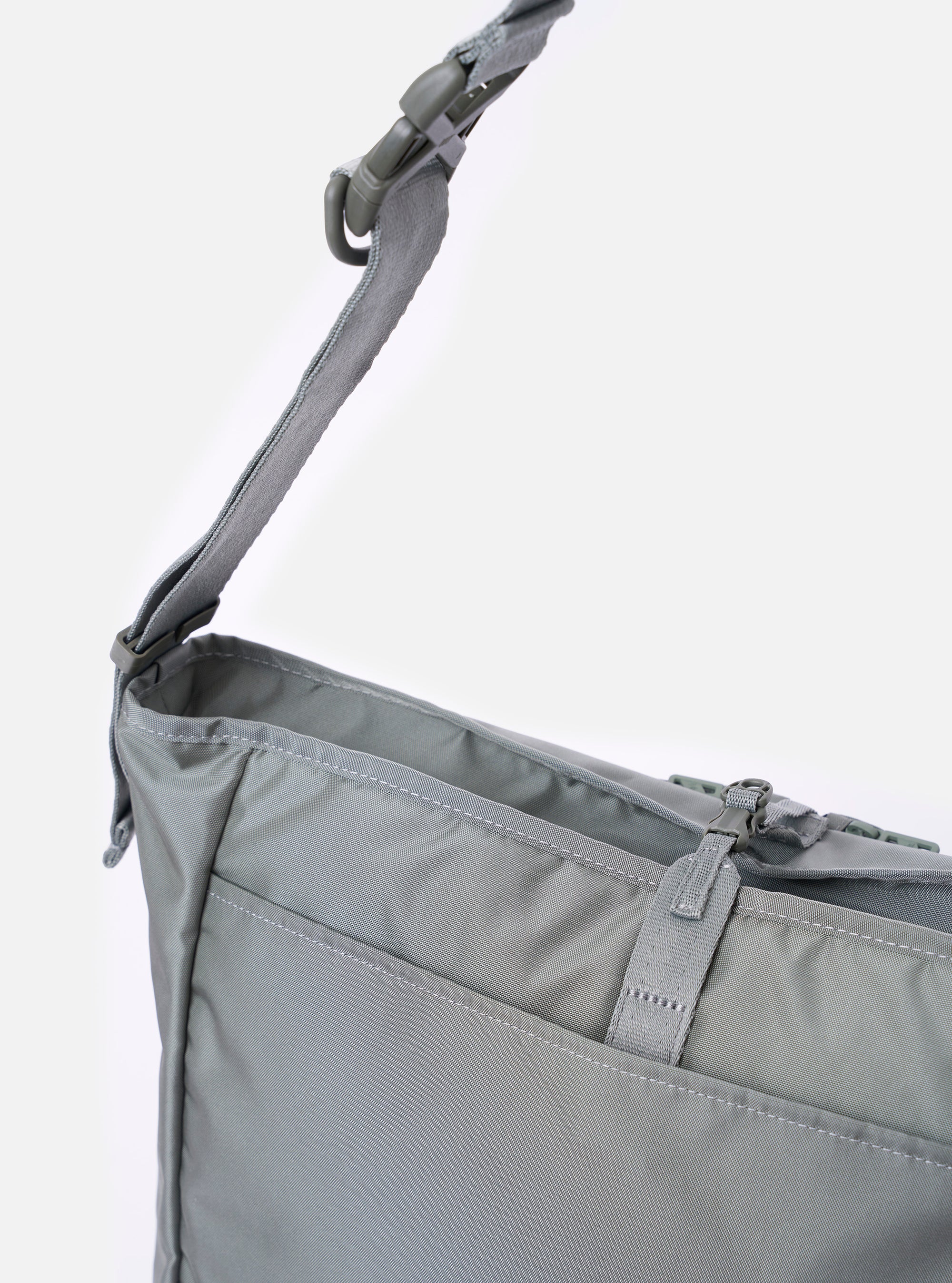 The F/CE.® Foliage Green Recycled Nylon 420 re/cor Courier Shoulder Bag is shown from the back as a flat lay against a plain white background. The image highlights the adjustable messenger-style shoulder strap with its plastic buckle and the clean, rectangular silhouette of the foliage green recycled nylon body.