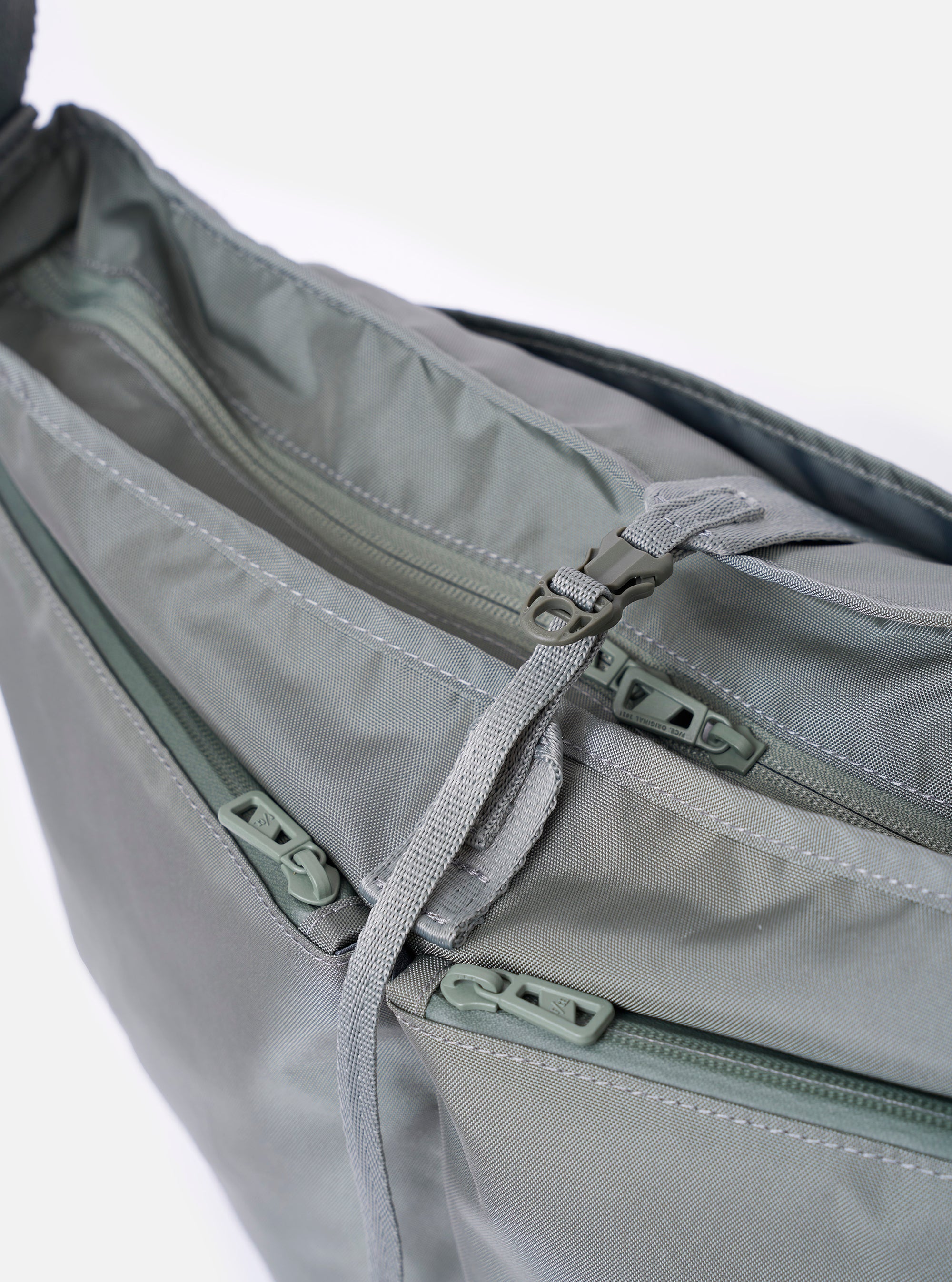 The F/CE.® Foliage Green Recycled Nylon 420 re/cor Courier Shoulder Bag is shown from a rear angle as a flat lay against a plain white background. The image highlights the adjustable messenger-style shoulder strap with its plastic buckle and the clean, structured back panel of the foliage green bag.