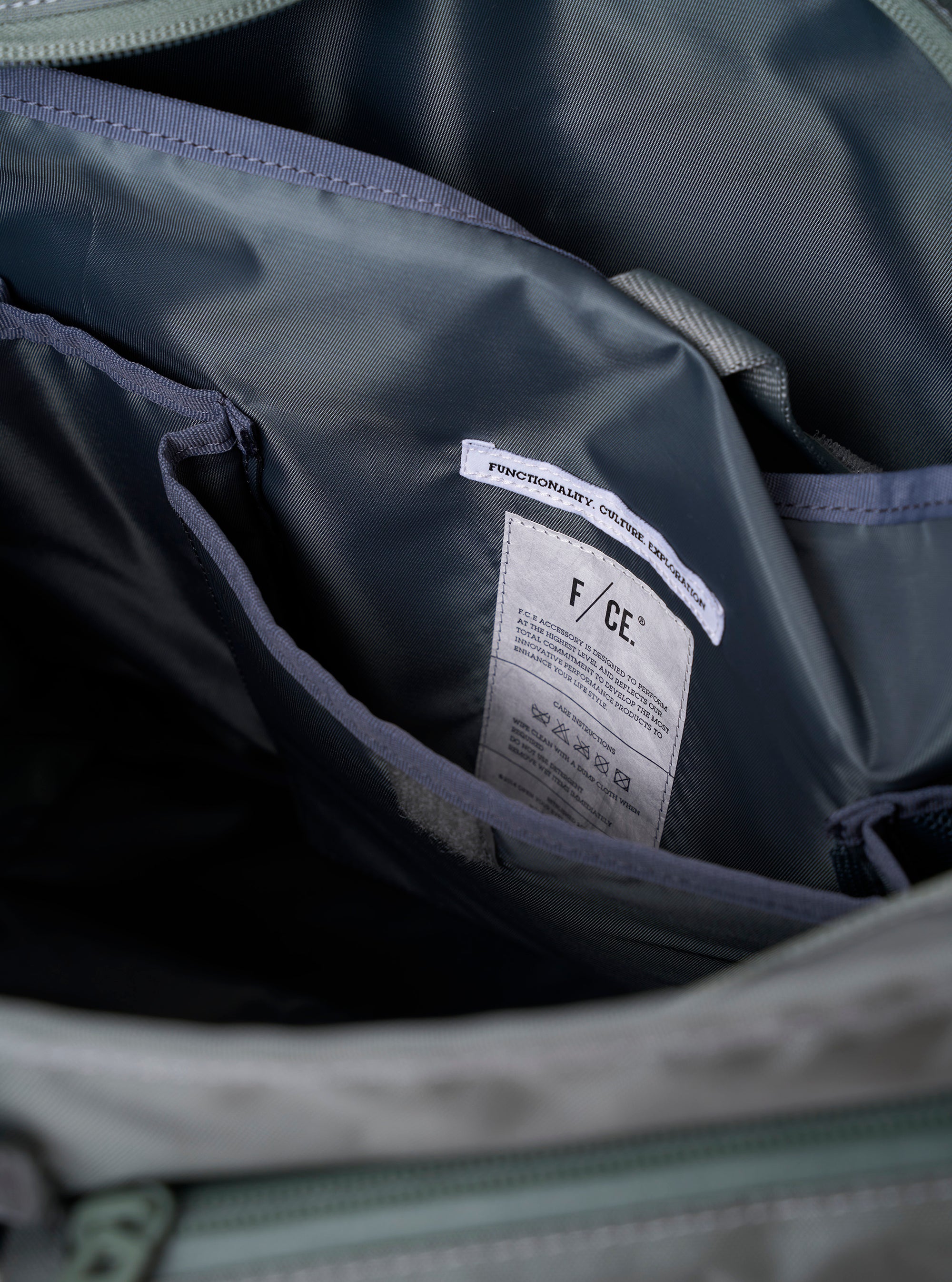 The F/CE. Foliage Green Recycled Nylon 420 re/cor Courier Shoulder Bag is worn by a model against a plain, light grey background. The model carries the bag across the body, highlighting its large, messenger-style silhouette and wide, adjustable shoulder strap. The foliage green recycled nylon fabric, front pocket details, and the way the bag sits snugly against the model's back are the prominent features of the image.