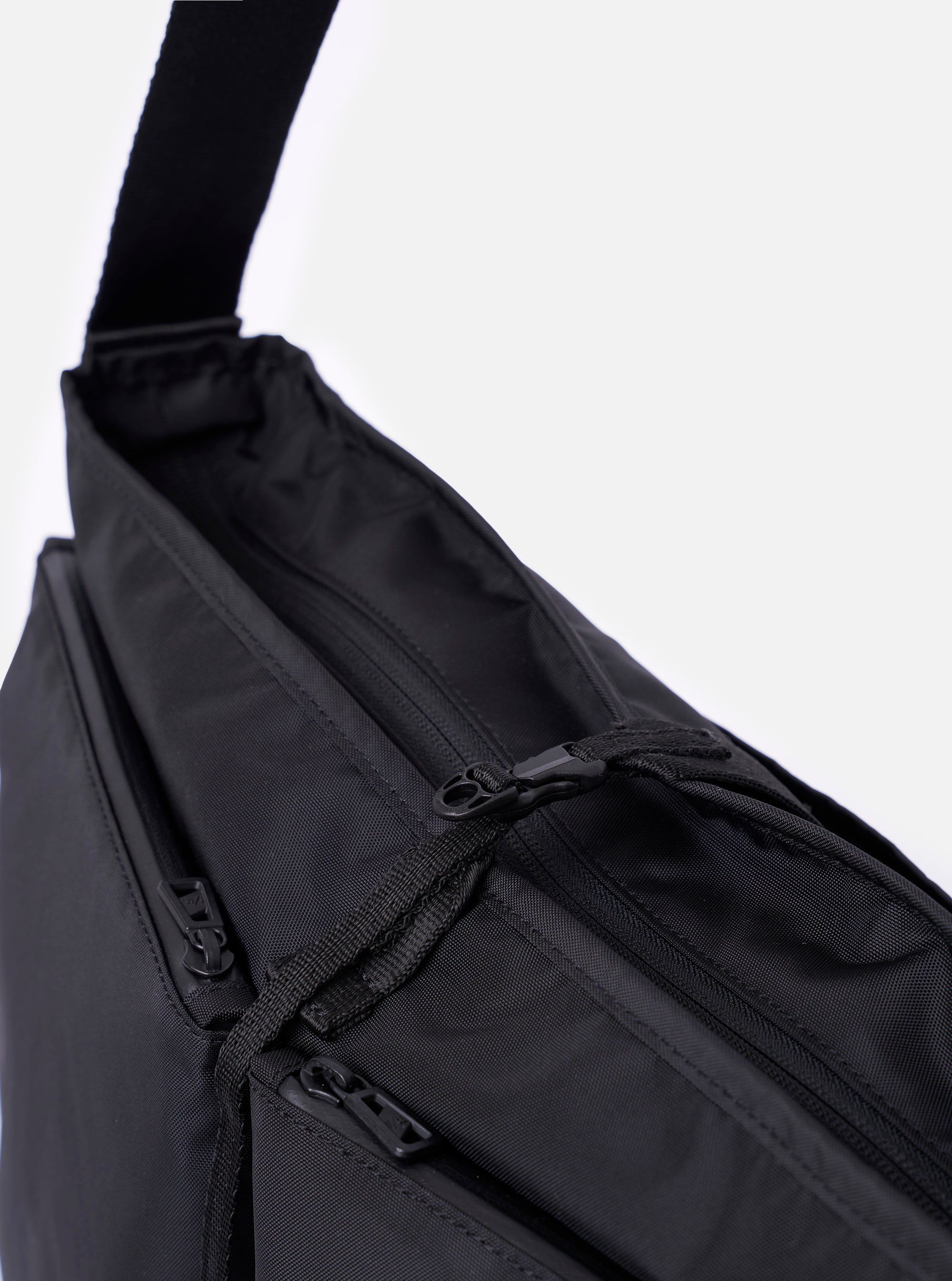 The F/CE.® Black Recycled Nylon 420 re/cor Courier Shoulder Bag is shown from a rear three-quarter angle as a flat lay against a plain white background. The image highlights the adjustable padded shoulder strap with a one-touch plastic buckle and the breathable mesh panel on the back of the bag. The black recycled nylon fabric has a smooth, technical appearance with visible tonal stitching.