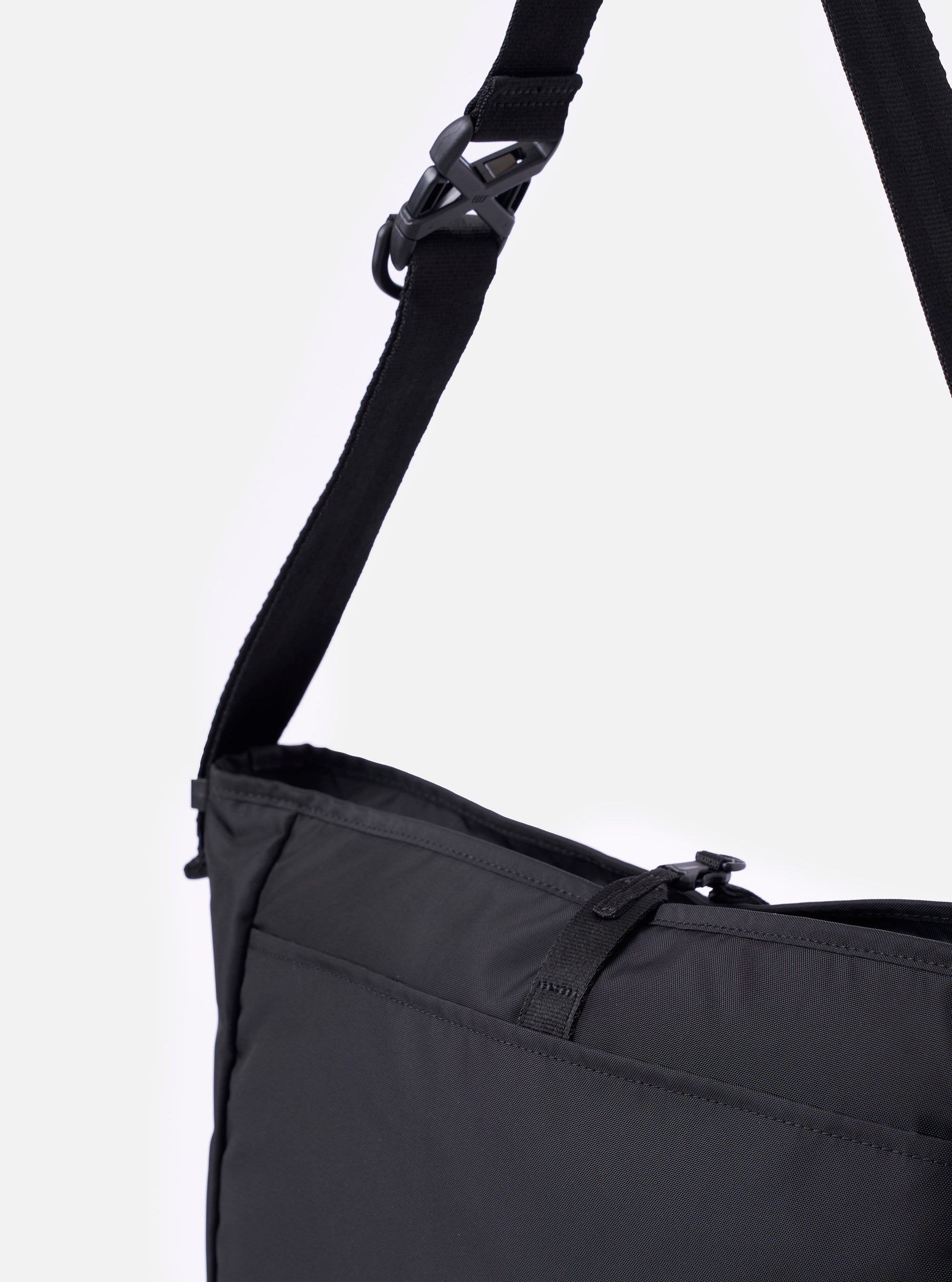 The F/CE.® Black Recycled Nylon 420 re/cor Courier Shoulder Bag is shown from the side in a studio shot against a plain white background. The image highlights the bag's depth and structure, featuring a large main zip compartment and a prominent helmet bag-inspired front pocket. The adjustable black nylon shoulder strap is attached with durable plastic hardware.