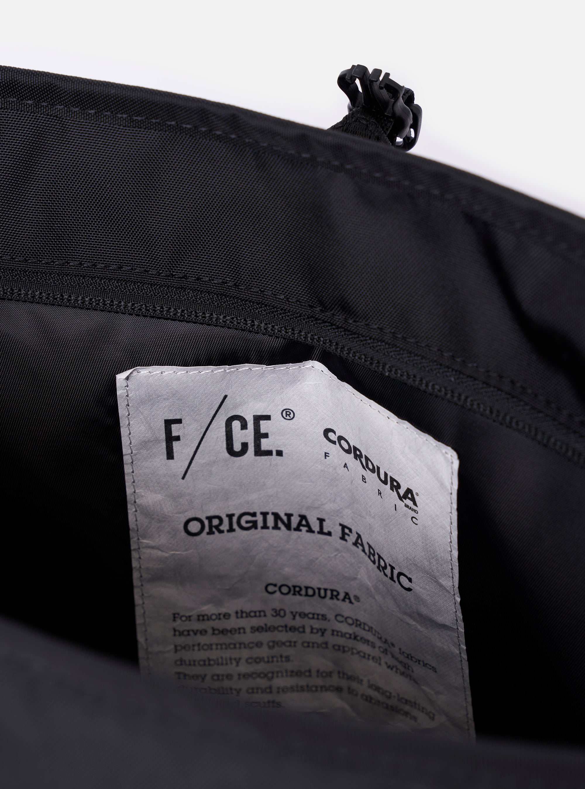The F/CE. Black Recycled Nylon 420 re/cor Courier Shoulder Bag is shown from a rear angle as a flat lay against a plain white background. The image highlights the padded mesh back panel, the adjustable shoulder strap with a one-touch plastic buckle, and the smooth black recycled nylon fabric.