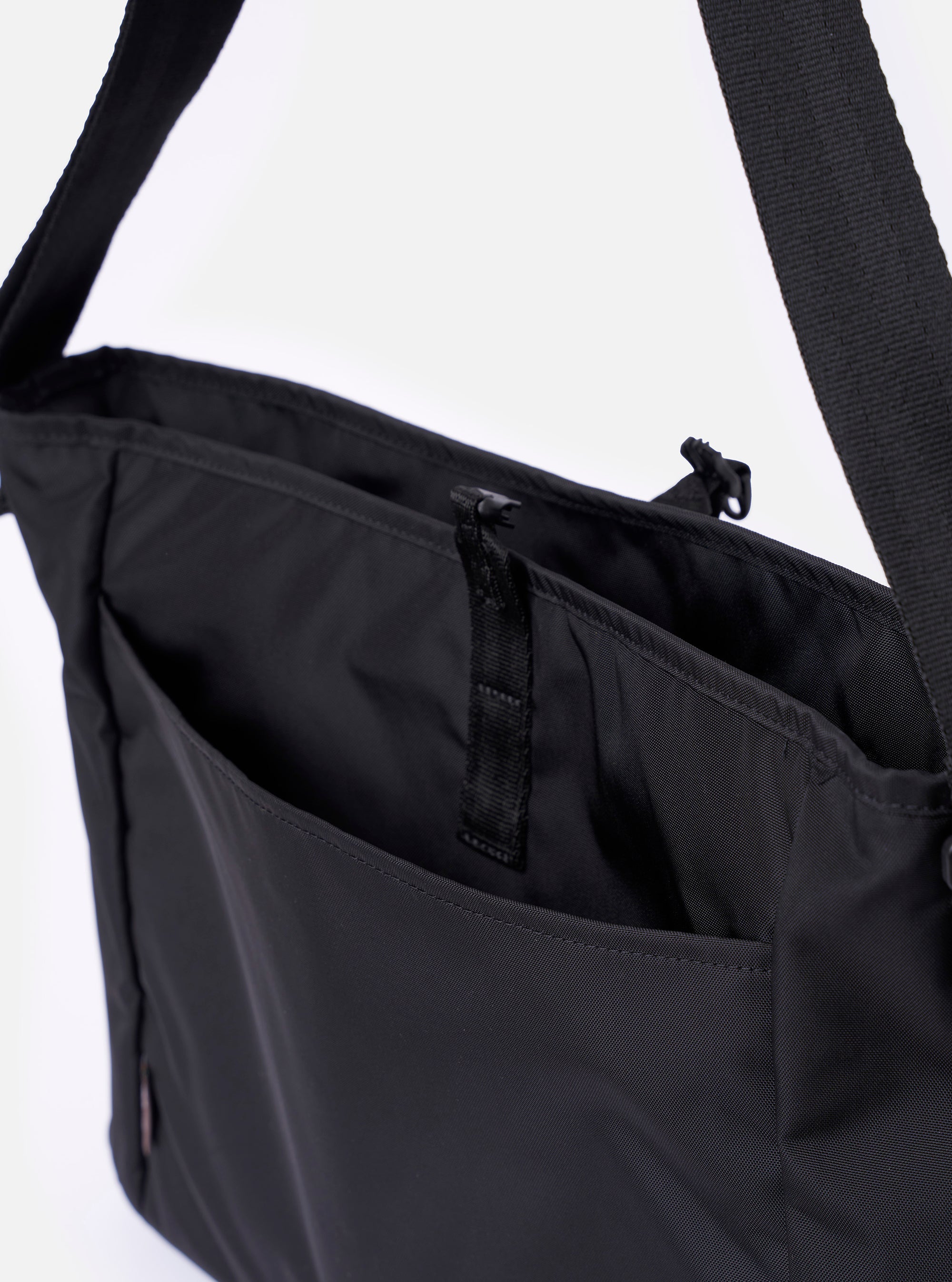 The F/CE.® Black Recycled Nylon 420 re/cor Courier Shoulder Bag is shown in a detail view as a flat lay against a plain white background. The image highlights the large, helmet bag-inspired front patch pockets with silver snap button closures and the smooth, technical texture of the black recycled nylon fabric.