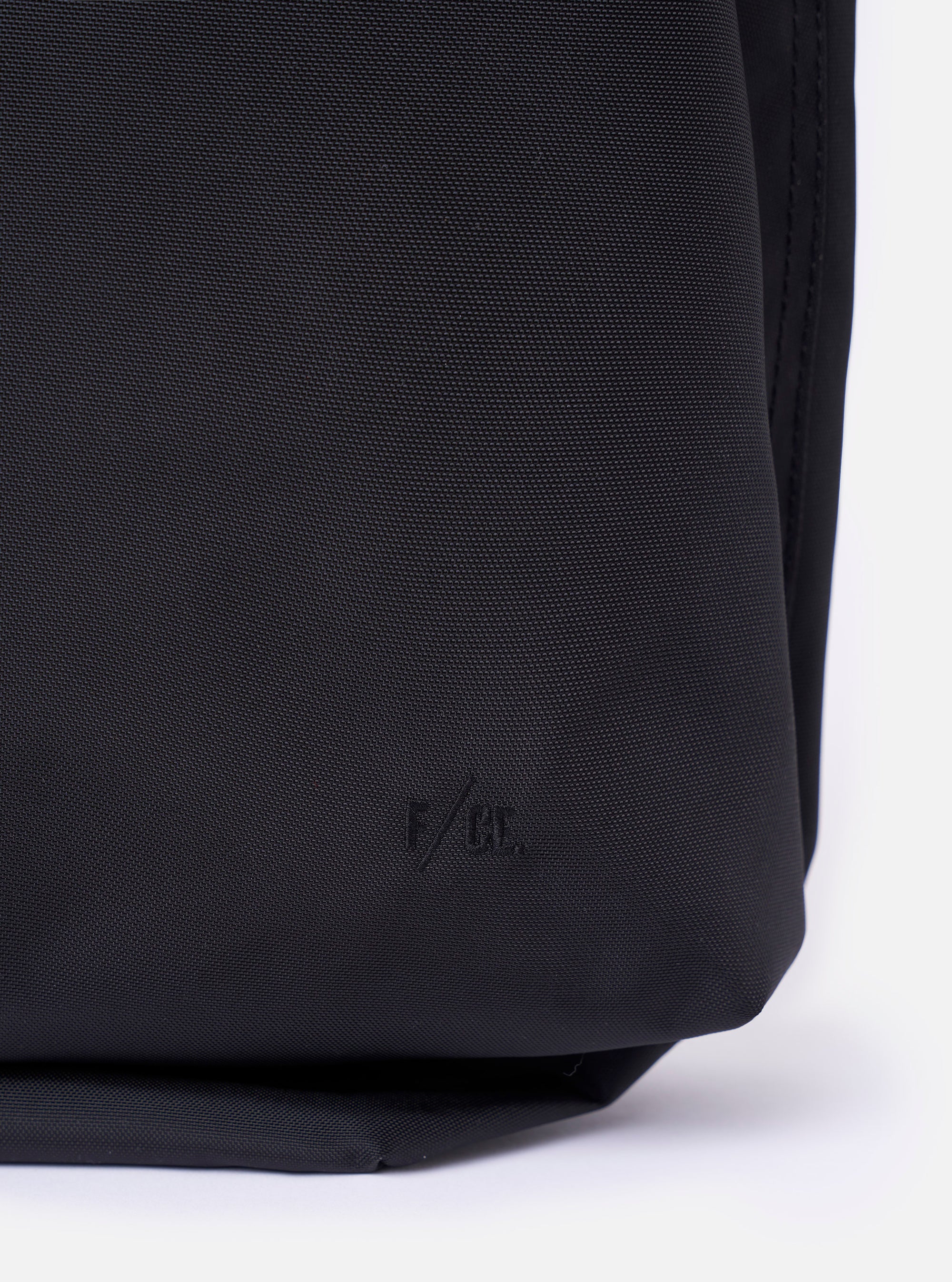 The F/CE.® Black Recycled Nylon 420 re/cor Courier Shoulder Bag is shown from a rear three-quarter angle as a flat lay against a plain white background. The image highlights the adjustable padded shoulder strap, the technical construction of the black recycled nylon fabric, and the various attachment points on the back of the bag.