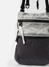 Close-up of the F/CE.® White Nylon Cordura Sil Portrait bag. The bag is two-tone, with a white nylon top and a black patterned bottom. Features black zippers and straps. Shot against a white background.