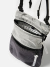Close-up of the F/CE.® White Nylon Cordura Sil Portrait bag, featuring a gray and black checkered pattern. The bag is partially unzipped, revealing the interior. Shot against a bright background.