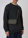 A model showcases the F/CE.® Charcoal Nylon Textured Twill Drawstring Sacoche against a plain backdrop. The bag, with a textured nylon finish, is worn crossbody.