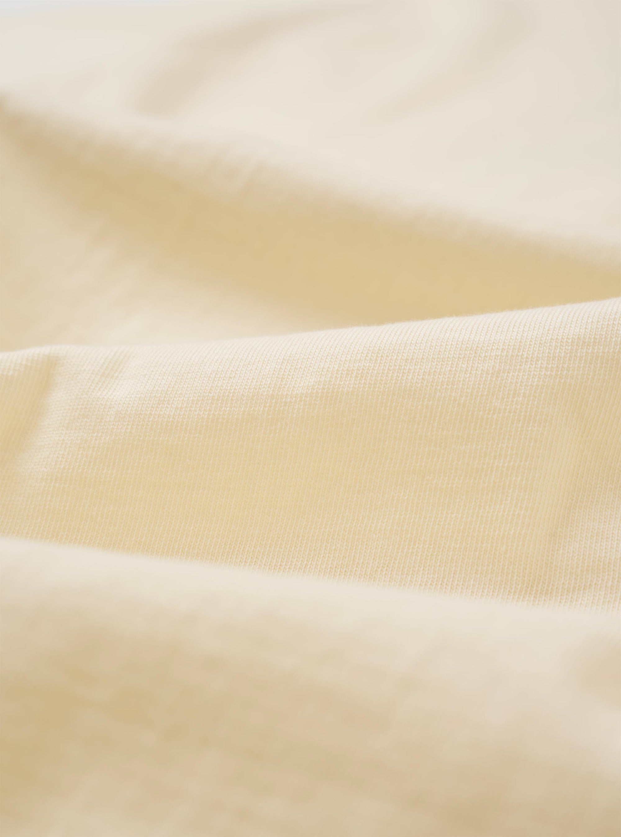 A close-up fabric swatch of the Kappy Cream Sundance Lounge Half Tee is shown, highlighting the soft, cream-colored cotton jersey material and its subtle knit texture. The fabric fills the entire frame.