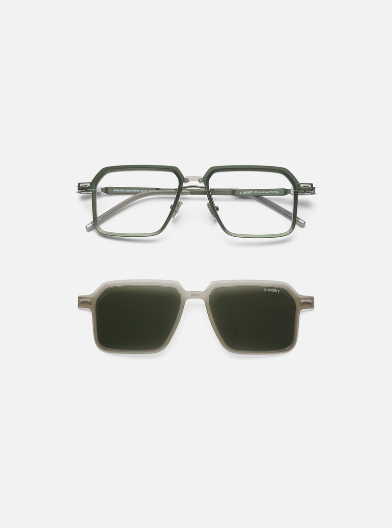 A. SOCIETY x Universal Works Olive/Green Kowloon Eyewear on a white surface. The glasses have an olive green frame and clear lenses, with a clip-on sunglass attachment.