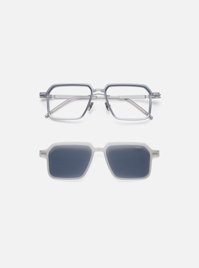 A. SOCIETY x Universal Works Silver/Grey Kowloon Eyewear on a white background. The frames are silver/grey. The sunglasses attachment has dark lenses.