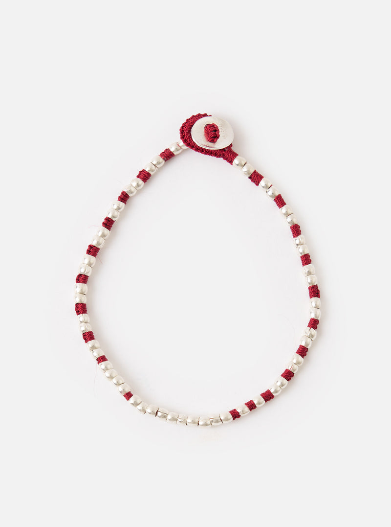 The Mikia Garnet Silver Beads Bracelet on a white surface. The bracelet features silver beads and garnet-colored string, with a silver button closure.