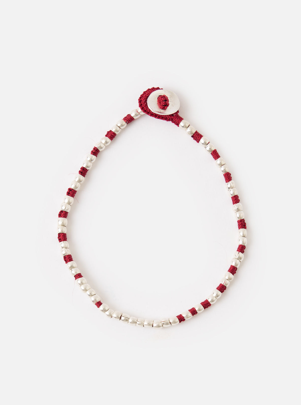 The Mikia Garnet Silver Beads Bracelet on a white surface. The bracelet features silver beads and garnet-colored string, with a silver button closure.