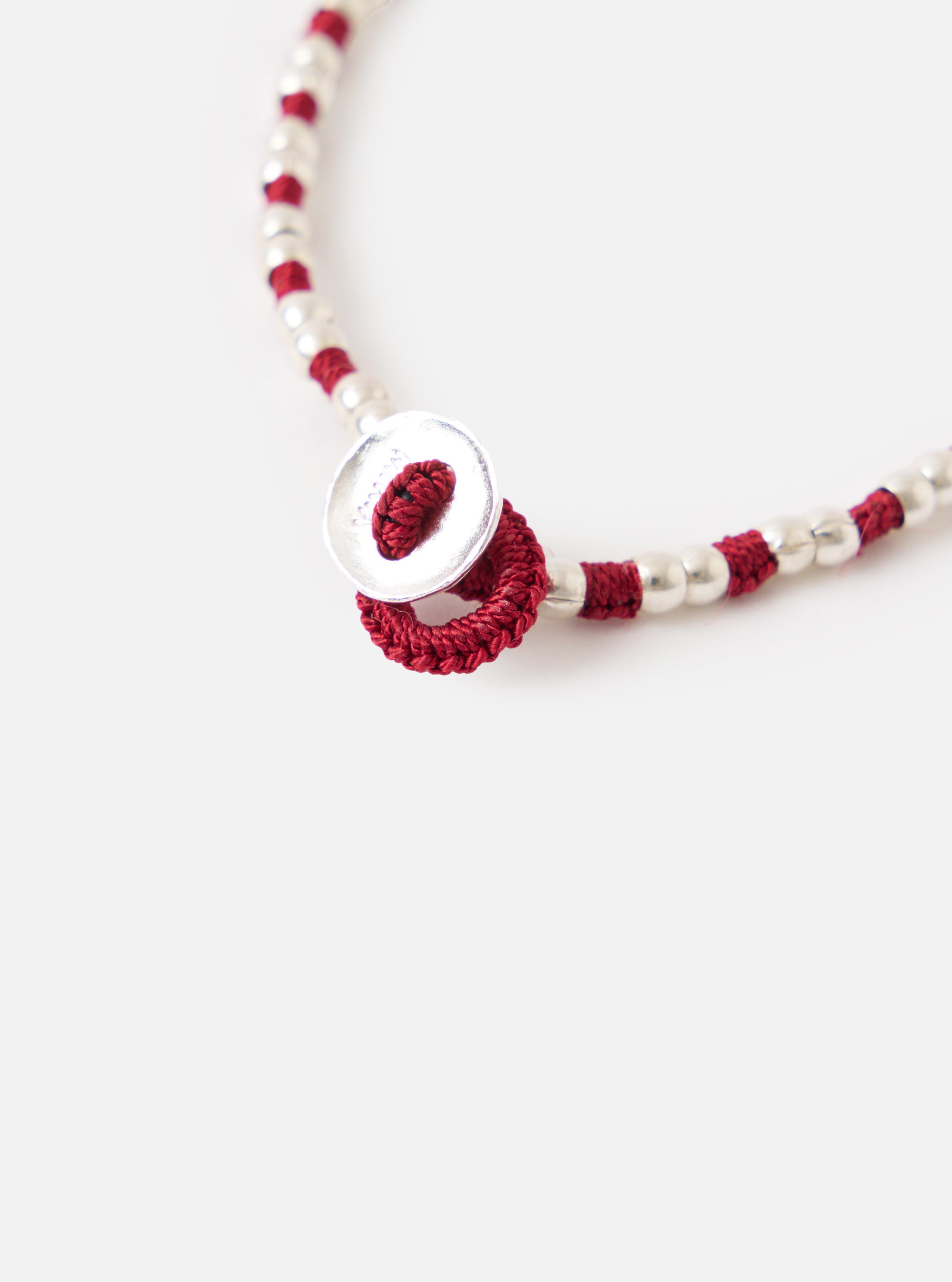 Close-up of the Mikia Garnet Silver Beads Bracelet on a white surface. Features silver beads, garnet-colored thread, and a unique silver button clasp.