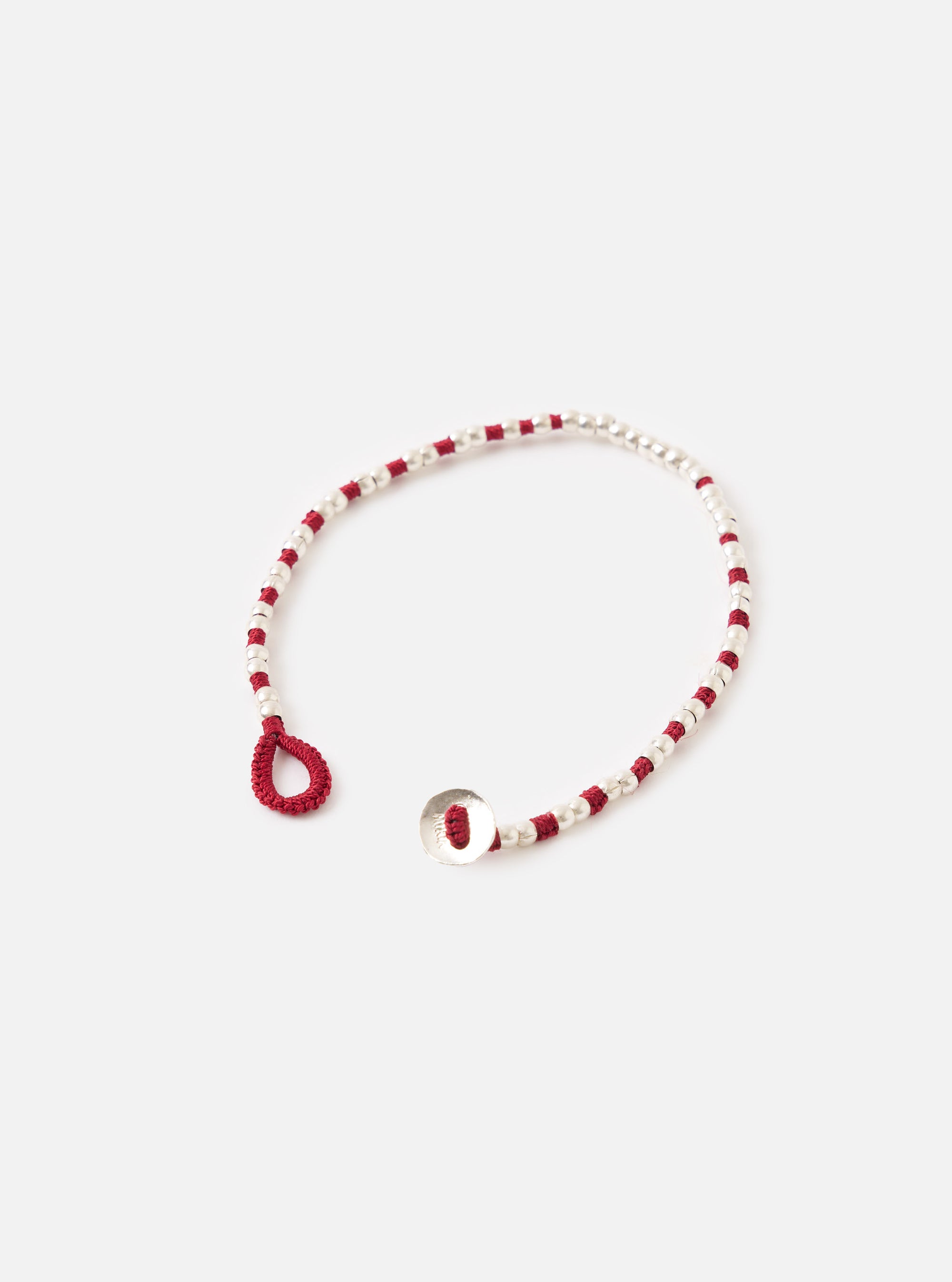 The Mikia Garnet Silver Beads Bracelet on a white surface. The bracelet features small silver beads and garnet-colored thread. The closure is a silver button and a garnet loop.