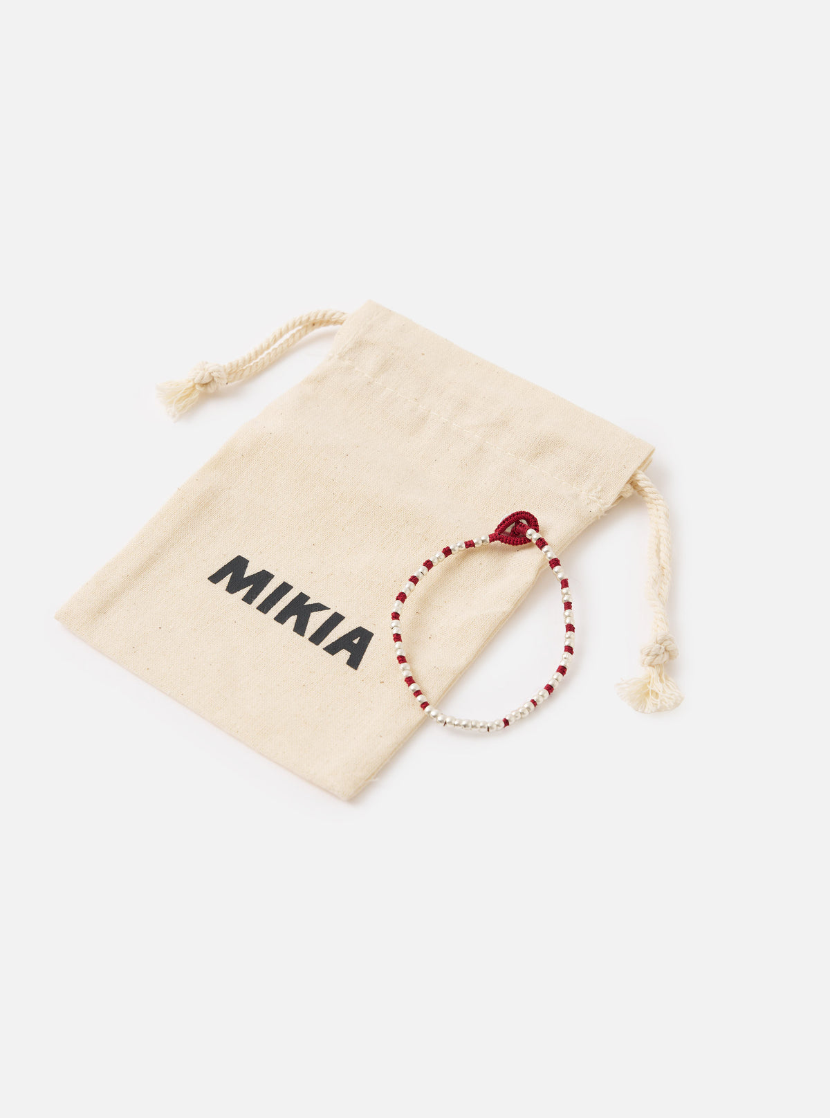 The Mikia Garnet Silver Beads Bracelet on a white surface with its branded beige pouch. The bracelet features red and silver beads.